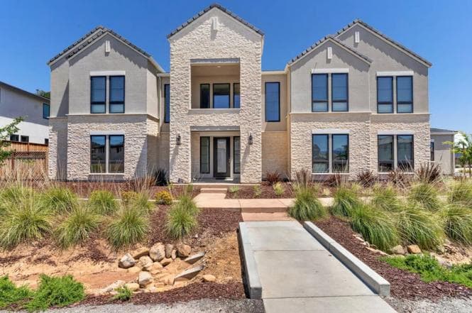 Front elevation of the two-story home in stone and stucco, with a recessed covered entry and a walkway from the street.