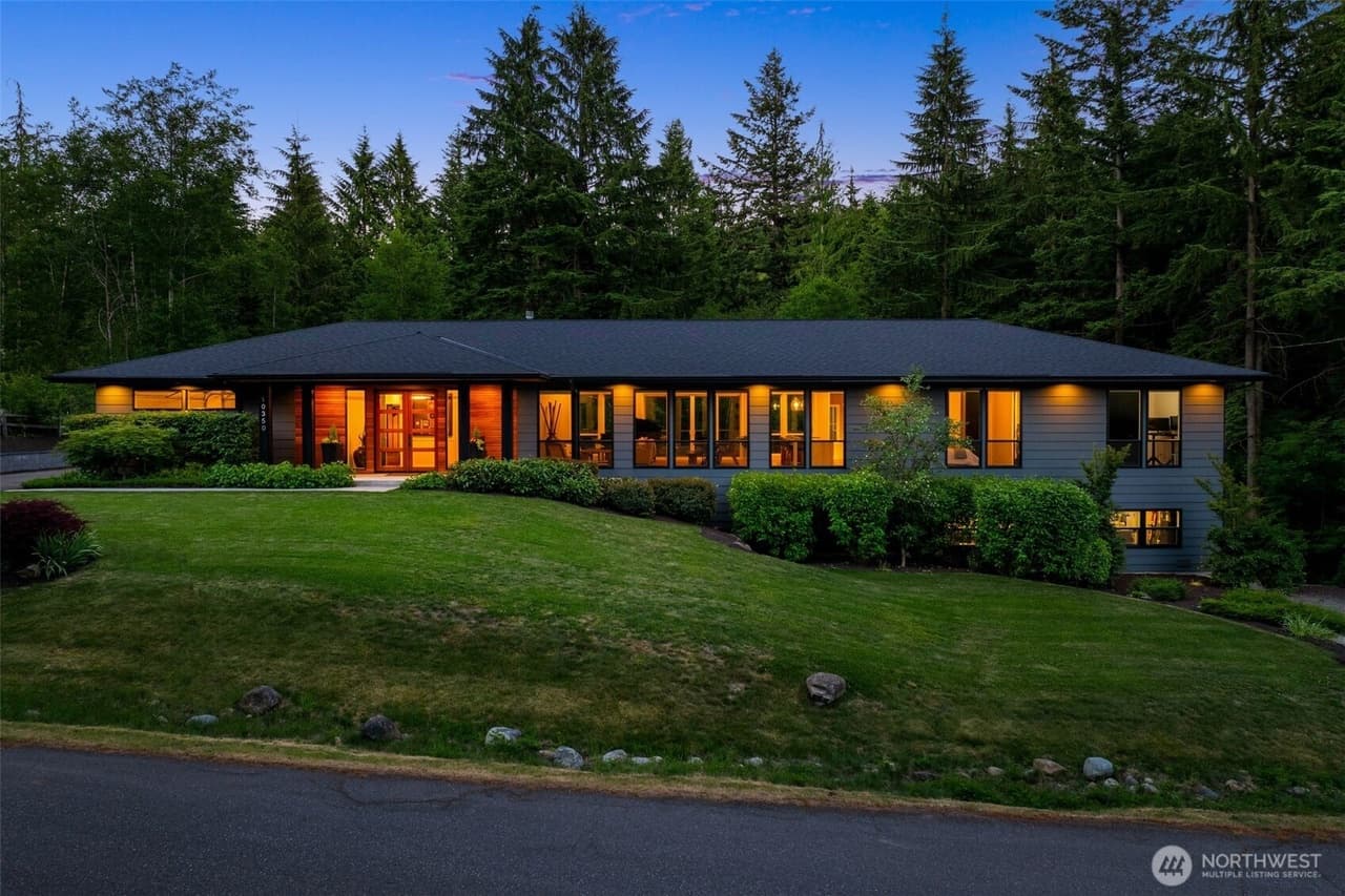 Front exterior of the single-level Snoqualmie home at dusk, with a landscaped lawn and forested backdrop.